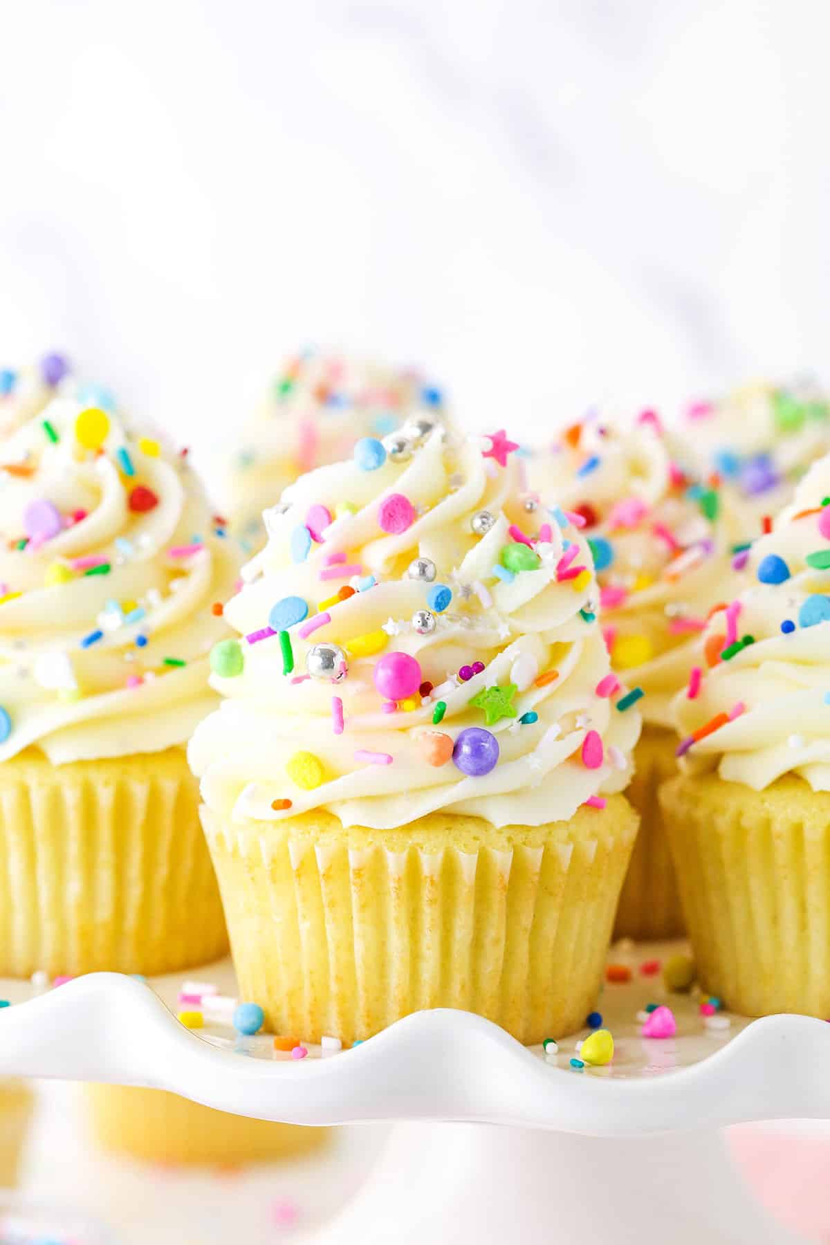 This Easy Homemade Vanilla Cupcakes recipe makes perfectly moist, irresistible cupcakes! Fluffy cupcakes topped with vanilla buttercream and sprinkles. Close up of vanilla cupcakes with vanilla frosting and rainbow sprinkles