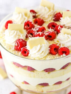 White chocolate raspberry trifle topped with swirls of whipped cream, fresh raspberries, and chocolate shavings.